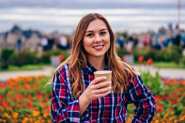 Café para llevar. Hermosa joven sosteniendo la taza de café y sonriendo en el parque