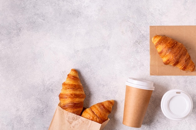 Café para llevar en un vaso de papel con croissants vista superior