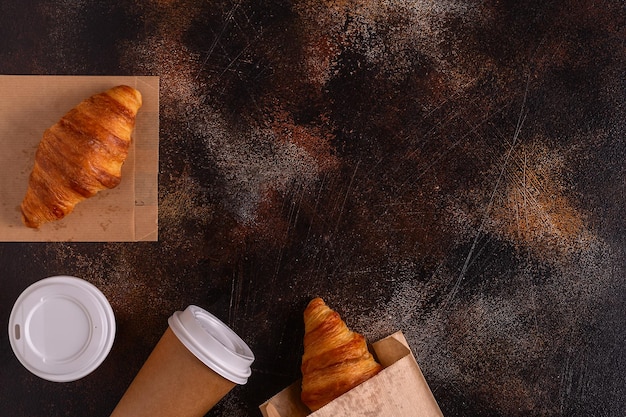 Café para llevar en un vaso de papel con croissants vista superior