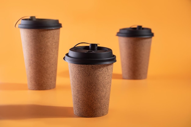 Café para llevar en un vaso de papel desechable sobre un fondo naranja con lugar para el texto