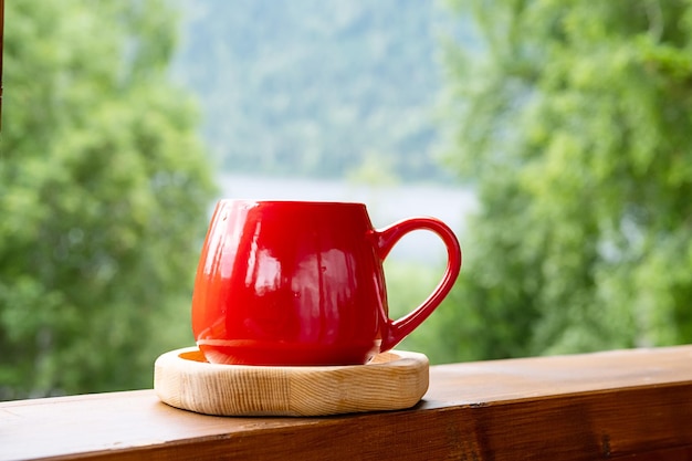 Café de la mañana en el jardín Taza roja sobre tabla de madera contra la naturaleza borrosa