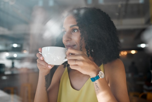 Café de la mañana pensando en una mujer negra y en la ventana de una cafetería con una persona en un restaurante Café sentado y una mujer africana con una bebida caliente de té disfrutando el día con felicidad y una idea