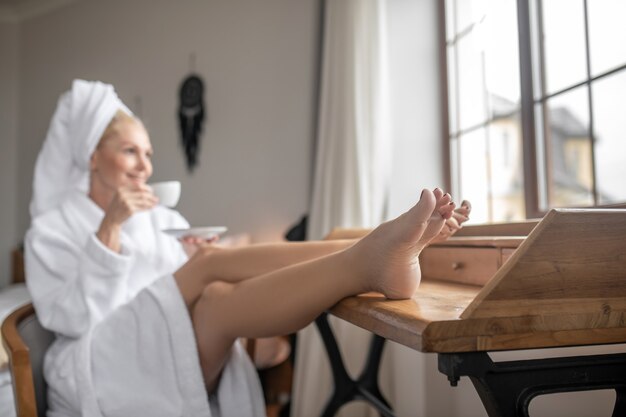 Cafe mañanero. Hermosa mujer en una túnica blanca tomando un café después del baño