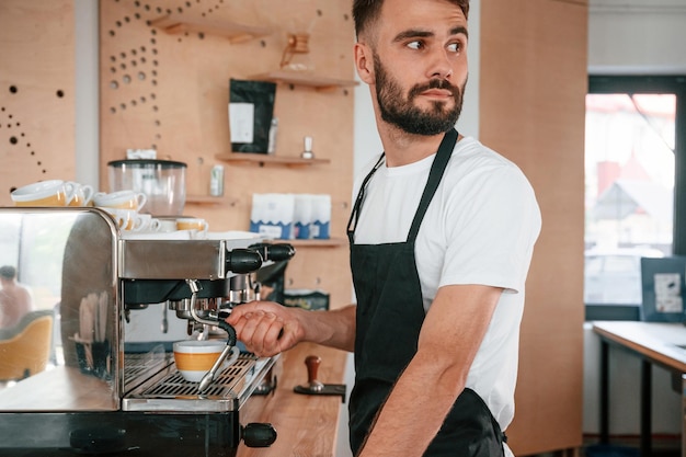 Café-Mitarbeiter in weißem Hemd und schwarzer Schürze bedient die Kaffeemaschine und ist drinnen