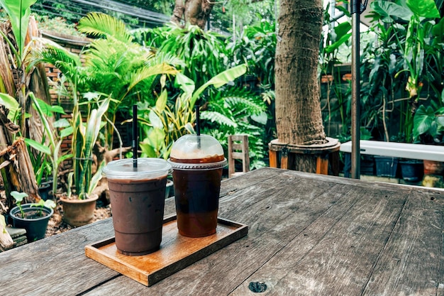 Café mocha frio em copo de plástico na mesa de madeira no café com vidro de fundo de planta e luz solar de café gelado com calda de chocolate ao leite na cafeteria