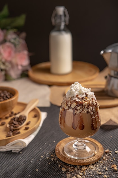 Café moka helado servido con cobertura de crema batida y jarabe de chocolate en copa de vino en lugar de mesa de madera