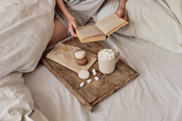 Café na cama. pernas femininas bem torneadas em meias quentes, bandeja de madeira para o café da manhã na cama. duas xícaras de café e marshmallows. o conceito de casa aconchegante. vista do topo