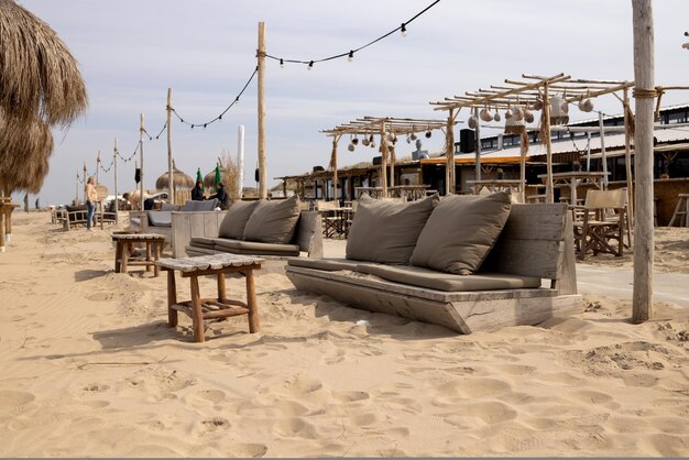 Café na praia de areia do mar com guarda-chuvas de junco poltronas de madeira e mesas pérgolas e lanternas