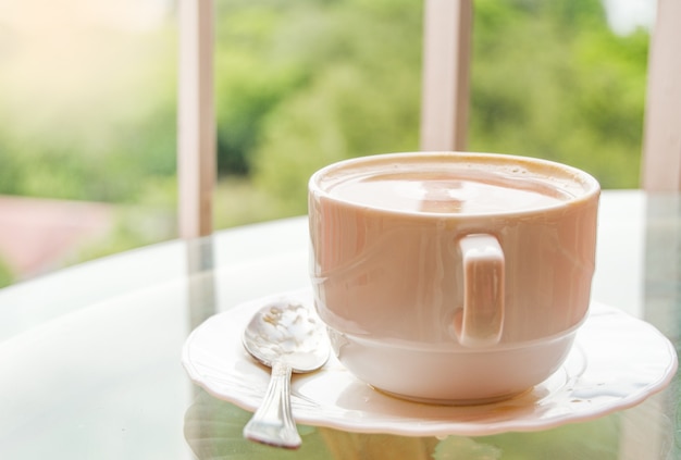 Café na xícara sobre uma mesa de vidro, varanda com vista para a natureza e o mar, um delicioso café da manhã ao nascer do sol.