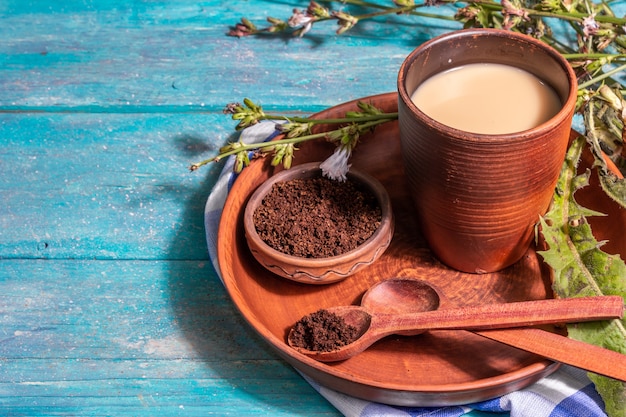 Café natural de chicória com flores frescas e pó. Bebida sem cafeína em vidro de cerâmica. Substituto alternativo para o café, a cafeína. Fundo de madeira turquesa, lugar para texto