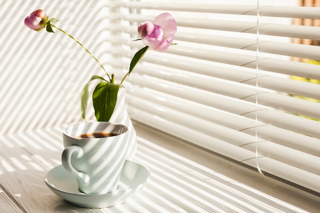 Café negro caliente y jarrón de flores en el alféizar de la ventana.