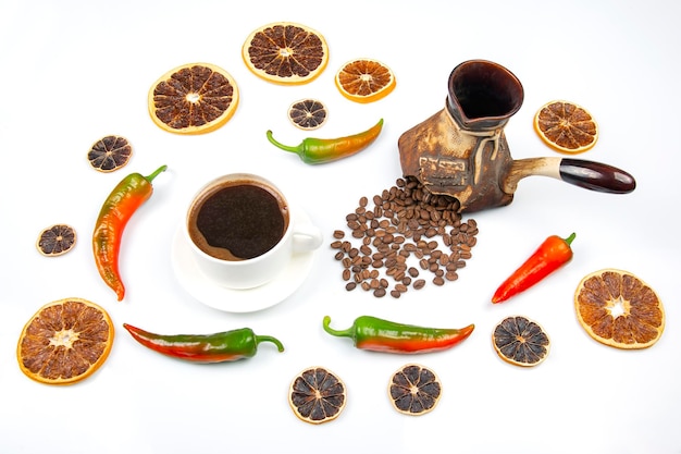 Café negro caliente recién hecho en una taza blanca sobre un plato blanco junto a un pavo de cerámica con granos de café. pimiento picante y limón