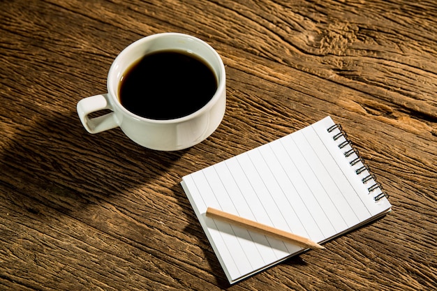 café negro caliente sobre una mesa de trabajo de madera y un cuaderno