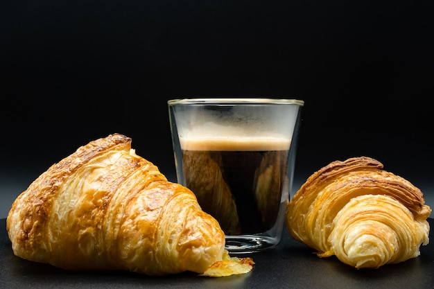 Café negro y croissant sobre fondo oscuro