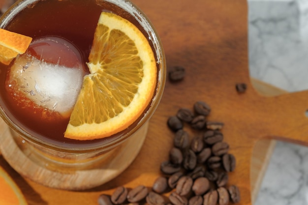 café negro helado frío mezclado con jugo de naranja y rodajas de naranja en vidrio sobre placa de madera