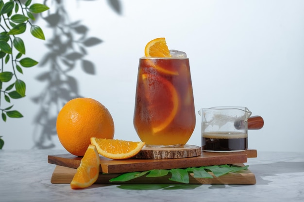 Foto café negro helado frío mezclado con jugo de naranja y rodajas de naranja en vidrio sobre placa de madera