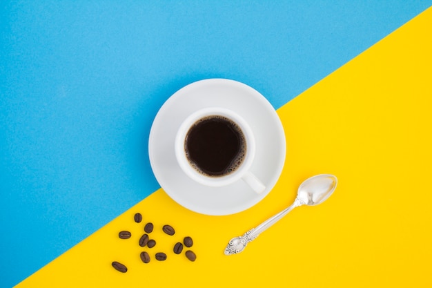 Café negro en la taza blanca y granos de café en el bicolor.