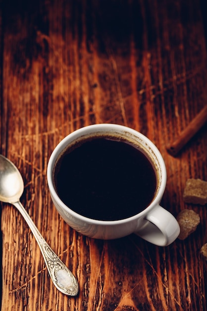 Café negro en taza blanca con palitos de azúcar y canela