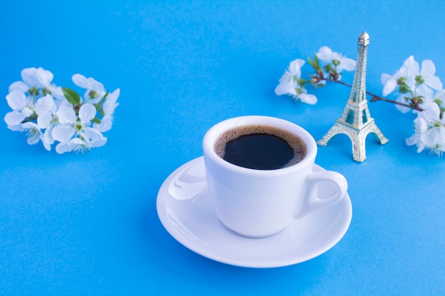 Café negro en la taza blanca, recuerdo de la torre eiffel y ramas en flor