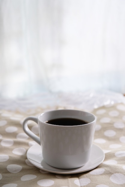 Café negro en una taza blanca sobre una mesa de tela de lunares.