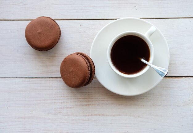 Café negro en taza blanca y tortas de macarrón en mesa de madera blanca