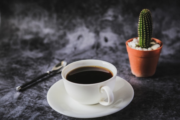 Café negro en una taza de café blanco y cactus colocados.