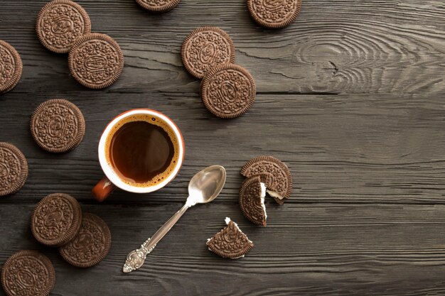 Café negro en la taza de cerámica marrón y galletas de chocolate en la madera negra