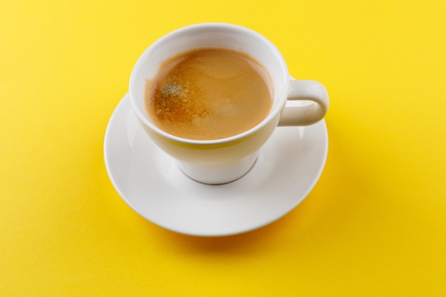 Café negro en una taza sobre un fondo amarillo