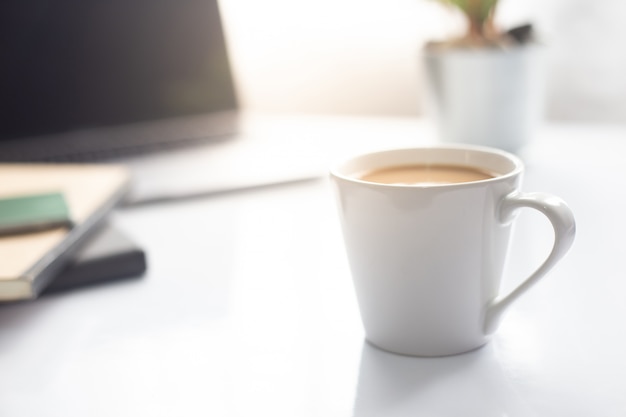 Café no notebook com laptop na mesa branca na luz do sol da manhã, espaço de trabalho