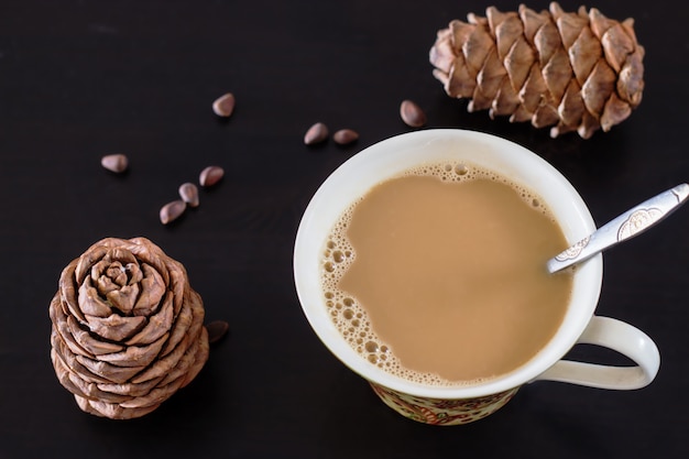 Café ou leite, chá chai com pinhão e leite vegan de cedro. Fundo de madeira preto e cones de pinheiro cedro siberiano. Vista do topo. Foco seletivo.