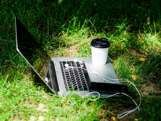 Café para viagem Coffee break ao ar livre Laptop smartphone moderno com fones de ouvido e xícara de café na grama verde Parque de verão Trabalhe e relaxe no ambiente natural Escritório verde É hora do café