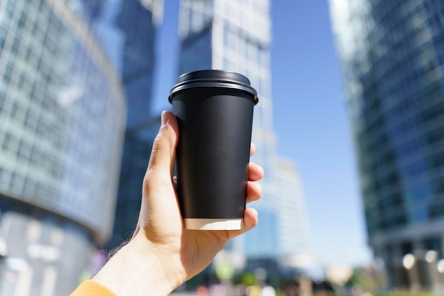 Café para viagem em um copo de papel Uma mão com uma bebida para ir ao fundo da rua da cidade Copo de papel