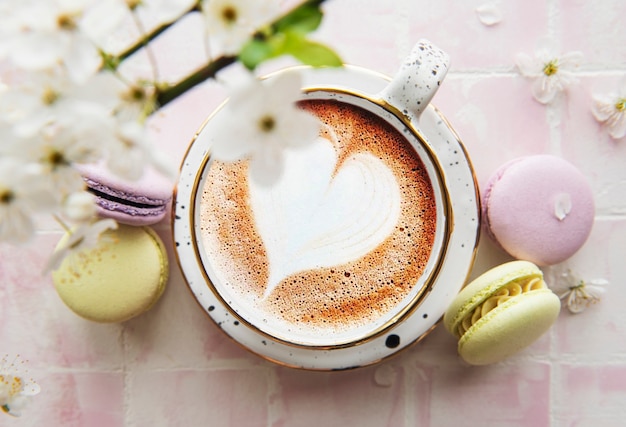 Café con un patrón en forma de corazón y postres dulces de macarrones sobre un fondo de mosaico rosa