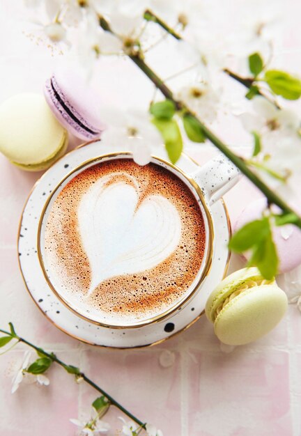 Café con un patrón en forma de corazón y postres dulces de macarrones sobre una superficie de azulejo rosa