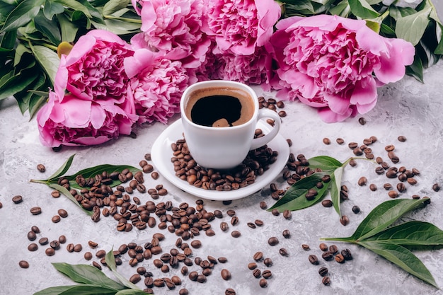 Café preto em uma xícara branca e peônias de cor rosa