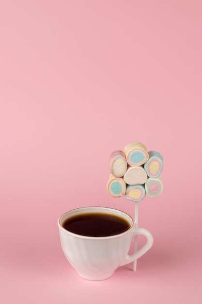 Café preto em uma xícara branca e um conjunto de marshmallows no palito em um fundo rosa. O conceito de um café da manhã divertido. Manhã feliz. Lugar para texto.