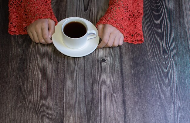 Foto café preto em uma xícara branca mãos em uma mesa de madeira de suéter de malha perfurada