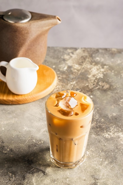 Café preto frio com cubos de gelo e leite em copo alto Bebida refrescante de café na mesa fundo cinza Closeup