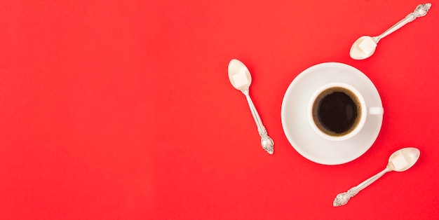 Café preto na xícara branca e colheres com açúcar no fundo vermelho Vista superior Copie o espaço