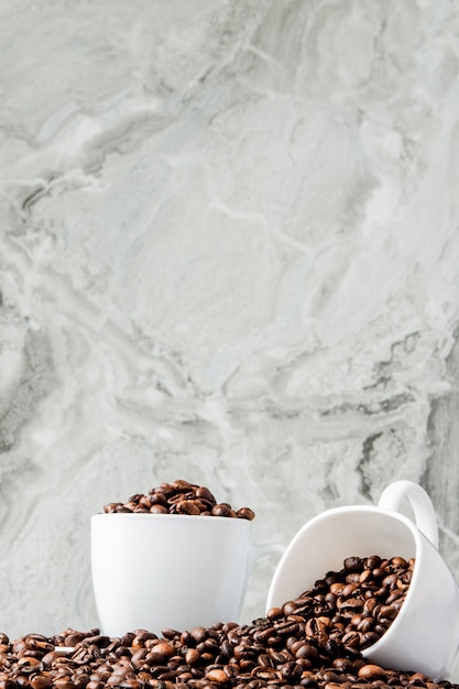 Café preto na xícara e grãos de café sobre fundo de mármore.