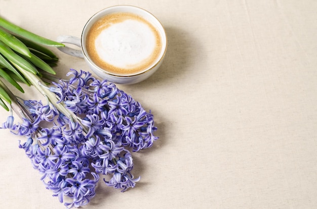 El café de primavera matutino en una taza de espuma junto a él yacen jacintos azules sobre un fondo beige