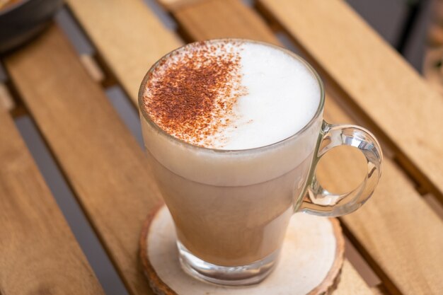 Café quente com leite em um copo sobre uma mesa de madeira com fundo natural Camada de café com leite macchiato