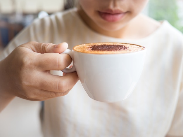 Café quente de cappuccino com leite no copo branco na mão pronto para beber e desfocar o fundo