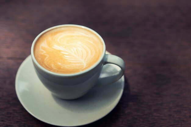 Café quente do Latte da arte em um copo na tabela de madeira na cafetaria.