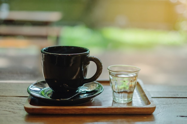 Café quente em copo preto com copo de água curto colocado na bandeja de madeira na cafeteria
