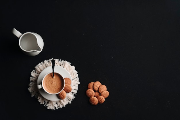 Café quente em uma xícara com alguns biscoitos em um prato e um fundo escuro. Copie o espaço. Vista do topo.