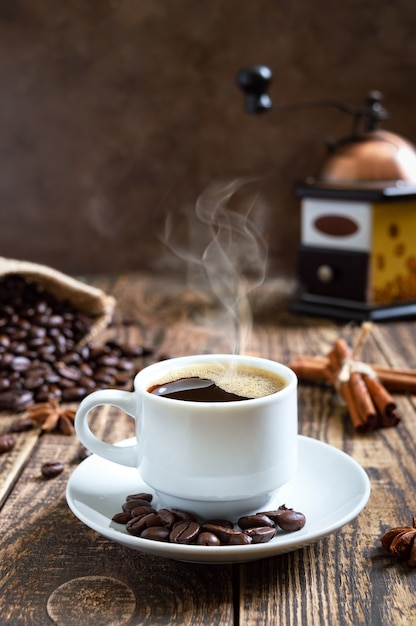 Café quente fumegante em uma velha mesa de madeira com grãos de café, moedor de café manual. visão vertical