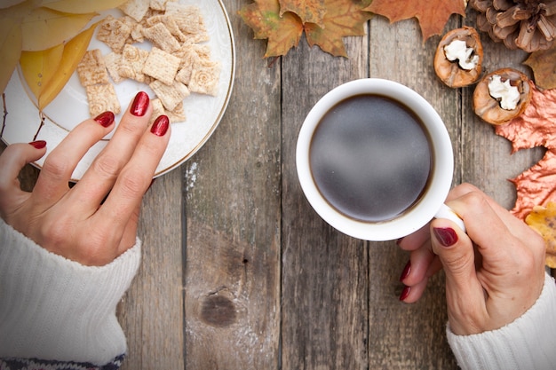 Café quente na mão de uma mulher, folhas de outono, uma blusa de malha quente, biscoitos