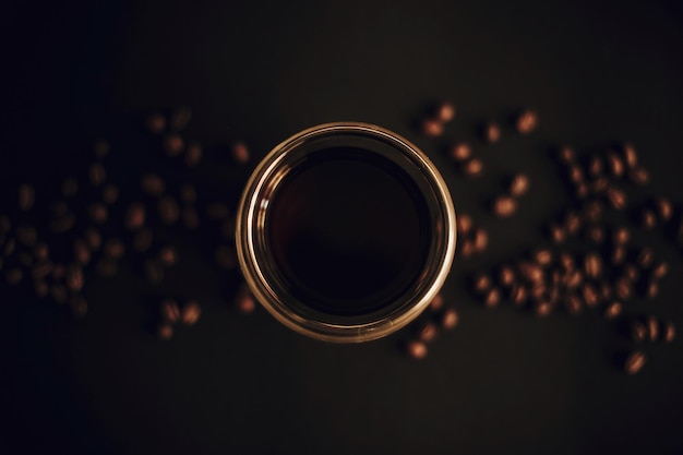 Café recién hecho en una taza de vidrio con granos de café sobre fondo negro plano Lay Goteo o filtro de café Imagen de mal humor oscuro Concepto de preparación de café
