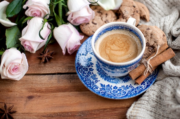 Café romatic em uma xícara em um fundo de madeira com uma manta, um buquê de rosas brancas e aconchego de outono. bom dia. vista superior. cópia spase